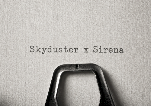 A black bag with a metal handle sits on a textured wall; over it text reads &ldquo;Skyduster x Sirena.&rdquo;