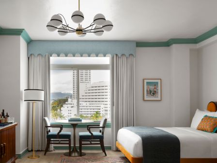 A modern bedroom with a ceiling chandelier, gray curtains, a large window, and a bed with pillows, plus wall art.