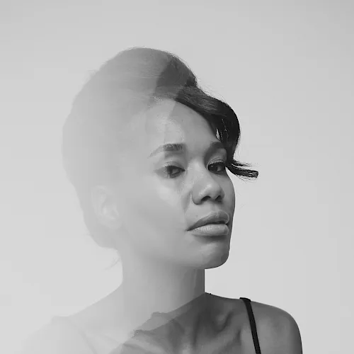 Black-and-white close-up portrait of a woman with hair tied back, turned sideways, wearing a black top with thin straps.