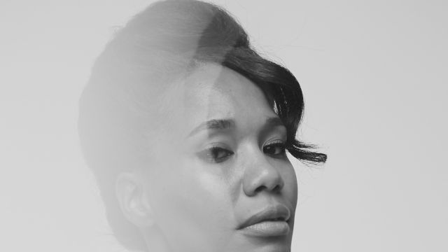Black-and-white close-up portrait of a woman with hair tied back, turned sideways, wearing a black top with thin straps.