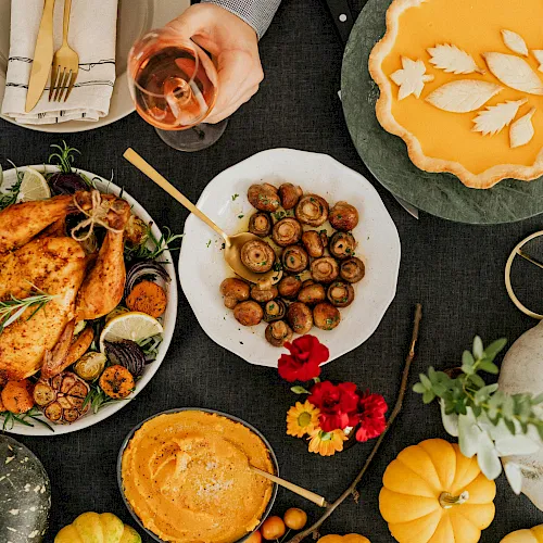 Roasted chicken, saut&eacute;ed mushrooms, pumpkin tart and pie on a table with glasses of wine and flowers.