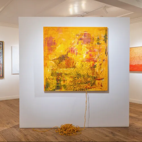 An art gallery with abstract paintings, including a large yellow canvas with cords draped on the wall and coiled on the floor.