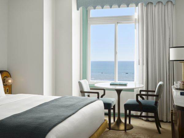 A hotel room with a bed, a table and chairs, a bar area, and a window offering an ocean view.