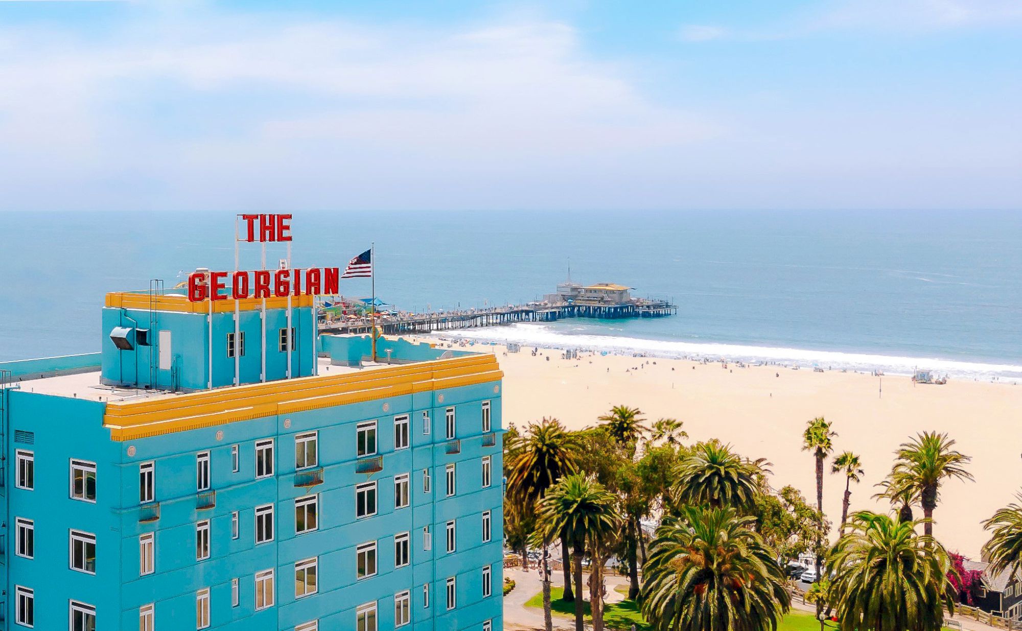 A beachfront scene with a blue building labeled "The Georgian," palm trees, and a pier extending into the ocean under a partly cloudy sky.