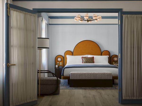 A stylish bedroom with a large bed, elegant lighting, and decorative headboard viewed through open double doors.