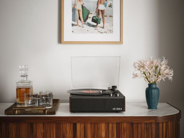 A wooden cabinet with a record player, a vase of flowers, drinks, and a beach-themed photo on the wall above.