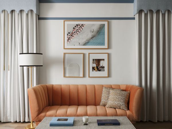 A stylish living room with an orange sofa, modern chandelier, artwork, floor lamp, geometric table, and neutral curtains.