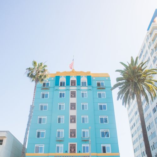 A bright blue building with yellow accents, surrounded by palm trees, under a clear sky. The setting conveys a sunny, tropical vibe.