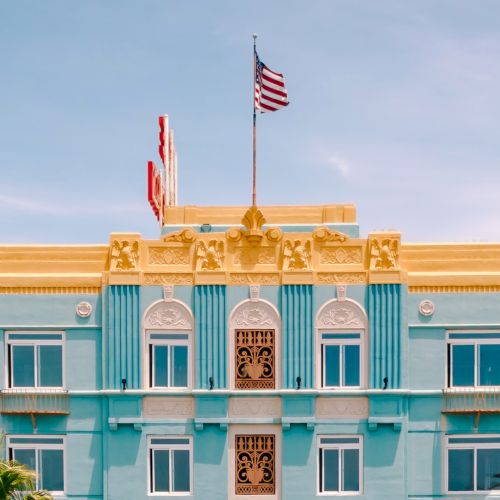 A vibrant building with blue and gold accents, an American flag on top, and surrounding modern structures under a clear sky.