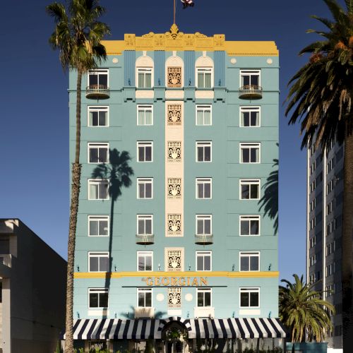 A colorful, multi-story building with an ornate design, palm trees, and a striped awning under a clear sky.