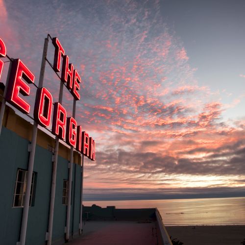 A neon sign reading "The Georgian" with a sunset over the ocean in the background.
