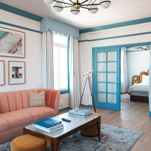 A cozy living room with a pink sofa, blue accents, a telescope, and glass doors leading to a bedroom.