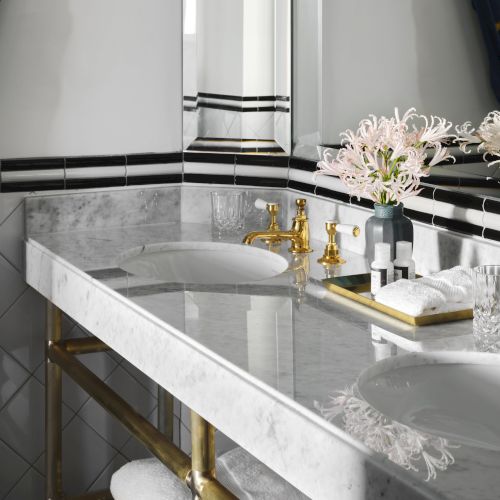 A luxurious bathroom features a marble countertop, double sinks, gold fixtures, flowers, and neatly folded towels on a tray.