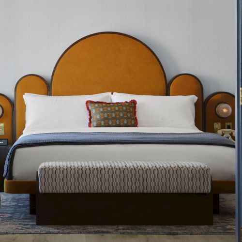 A stylish bedroom features a large bed with orange and white linens, a unique headboard, and two round lamps on nightstands beside the bed.