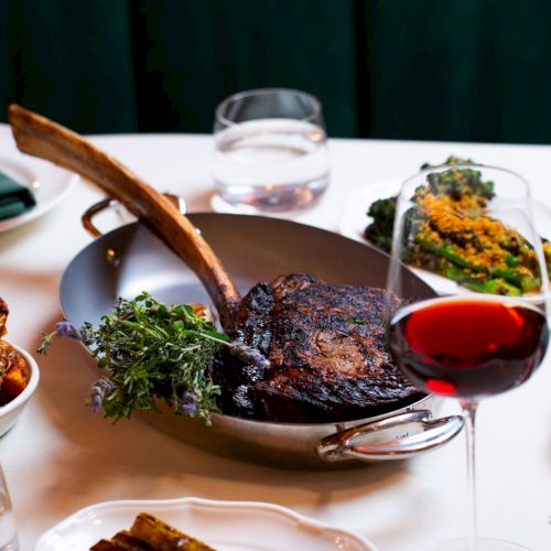 A table with a cooked meat dish, asparagus, red wine, glasses, and "The Georgian, Santa Monica" text above.