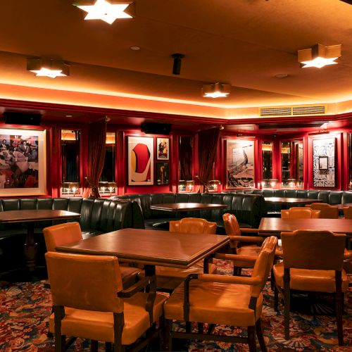 The image shows a warmly lit, elegant restaurant interior with cushioned seating, wooden tables, and framed art on the walls.