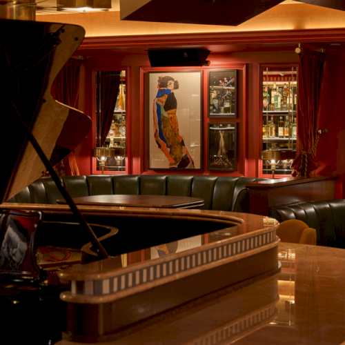 A dimly lit bar features a grand piano, rounded seating, and art on the walls, creating a classy and intimate atmosphere.