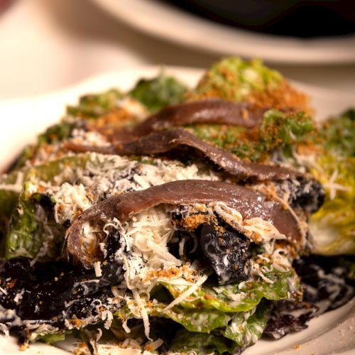 The image shows a Caesar salad topped with anchovies and grated cheese, served on a white plate.