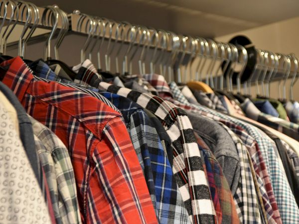 A variety of shirts with plaid and patterned designs are hanging on a clothing rack, neatly organized.