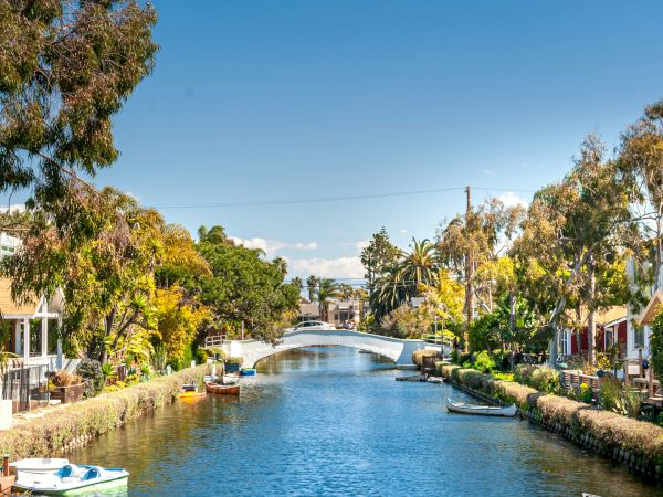 A tranquil canal lined with trees and houses, under a clear blue sky, with small boats along the water's edge.