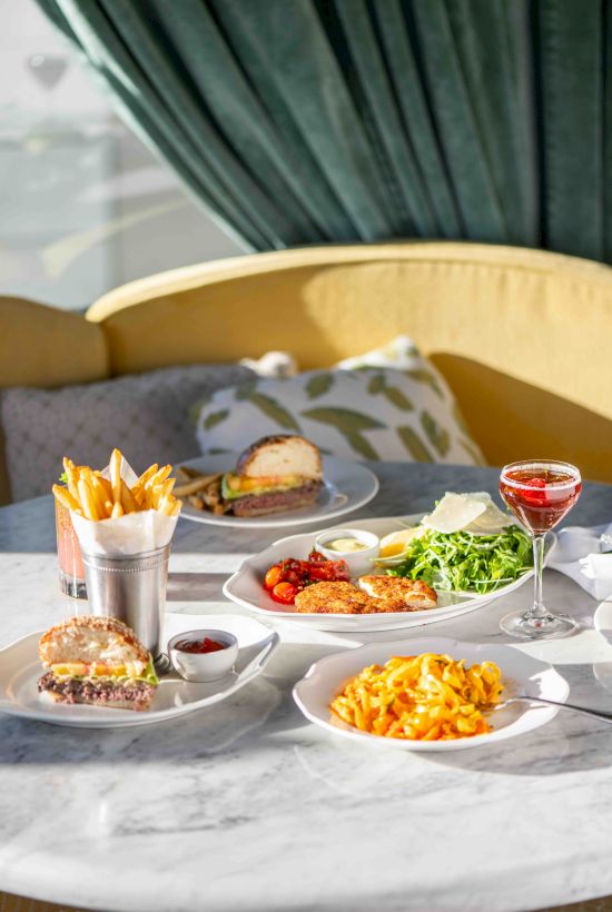 An outdoor table set with burgers, fries, salad, pasta, sauces, and a glass of red wine.