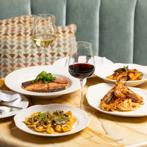A fine dining scene with plates of pasta and steak, wine glasses, and a cozy booth setting.