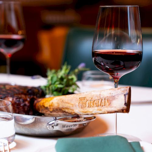 Two wine glasses, a roast with herbs, and a baguette on a white tablecloth at a cozy dinner.