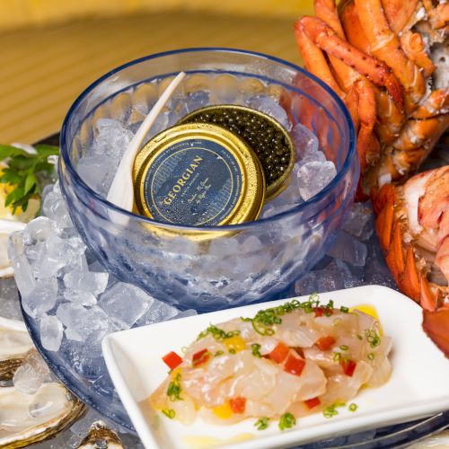 A seafood platter with oysters on the half shell, shrimp, lobster tails, ice bucket with champagnes, and a small plate of white fish sashimi, all beautifully arranged.
