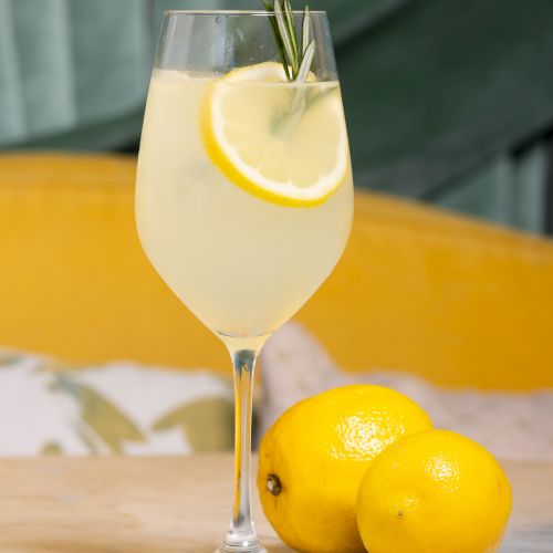 A refreshing lemon spritz with a lemon slice and rosemary garnish in a stemmed glass, bright and summery.