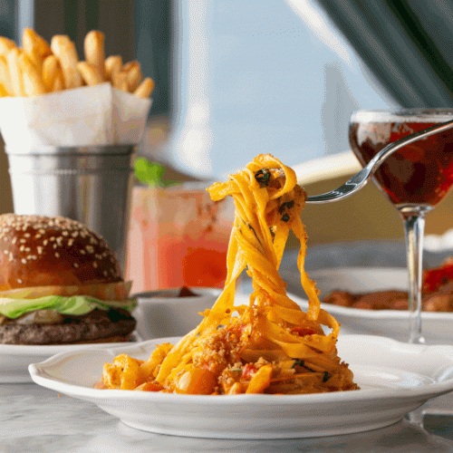 A juicy burger with fries and a drippy cheese sauce, plus a side of nacho-like chips, and a cocktail on a sunny patio.