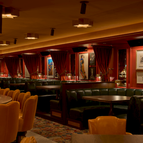 A dimly lit restaurant or lounge with red velvet curtains, brown leather booths, and framed art along the walls, creating a cozy, upscale vibe.