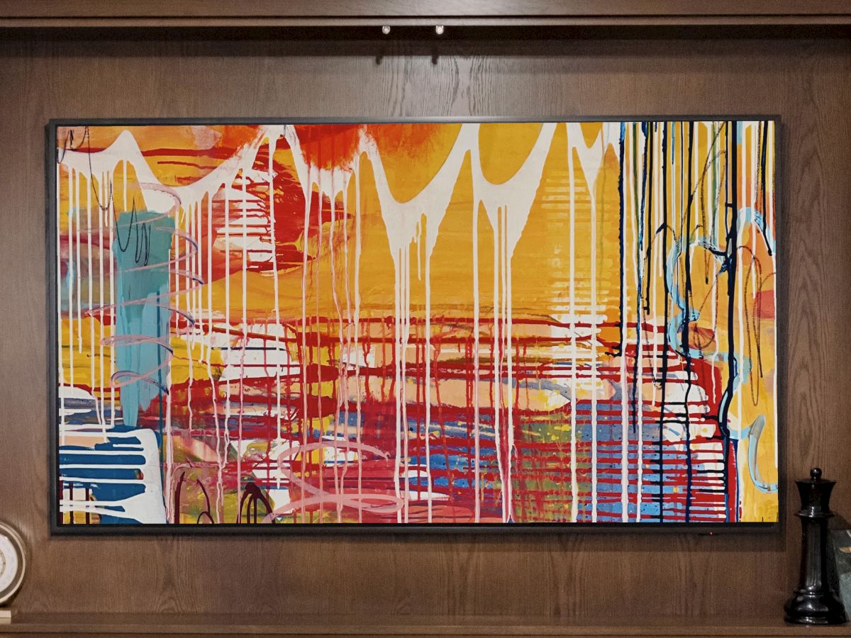 Abstract colorful painting with dripping white lines on a warm-toned background, displayed in a wood-framed wall niche with small decor items at sides.