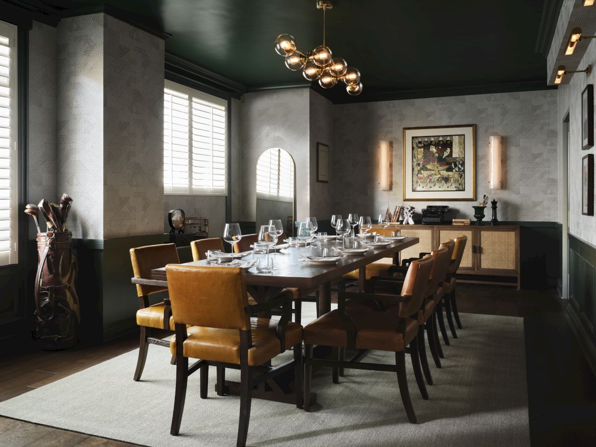 A formal dining room with a long wooden table, tan upholstered chairs, modern black walls, a sideboard, framed art, and contemporary chandelier lighting.