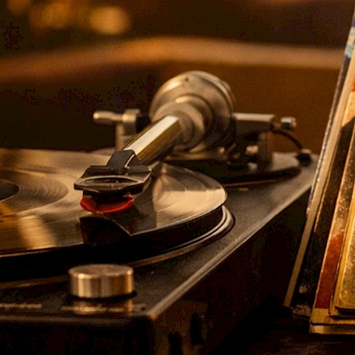 A vintage turntable records a vinyl with a tonearm playing; a spinning record, with a dusty, warm-toned close-up, on a wooden shelf.