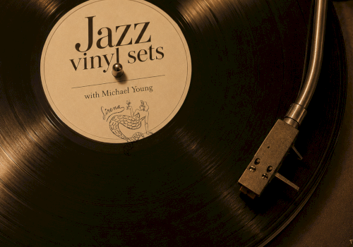 A close-up of a spinning vinyl record on a turntable, label reads &ldquo;Jazz vinyl sets,&rdquo; with text &ldquo;Sundays 5PM-9PM&rdquo; and a signature at the bottom.