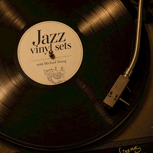 A close-up of a spinning vinyl record on a turntable, label reads &ldquo;Jazz vinyl sets,&rdquo; with text &ldquo;Sundays 5PM-9PM&rdquo; and a signature at the bottom.