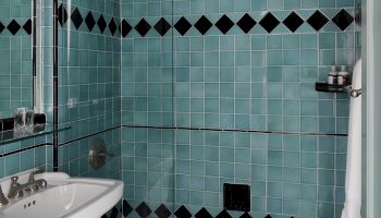 Tiny turquoise tiled bathroom with a glass shower door, pedestal sink, and a black-and-teal diamond border.