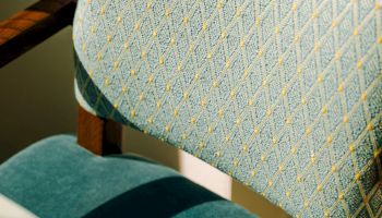 A vintage upholstered chair with teal and patterned fabric, wooden armrests, and a light green wall in the background, likely in a living space.