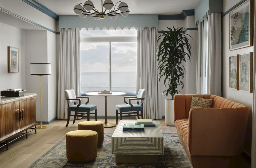 A stylish living room with a teal accent, large window, orange sofa, tall plant, striped curtains, and modern coffee table setup.