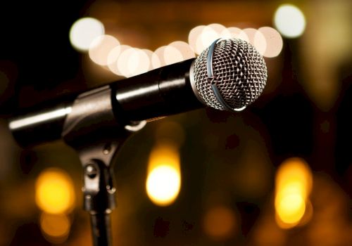 A close-up of a microphone on a stand, ready for a performance, with warm bokeh lights in the background.