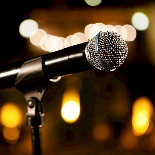 A close-up of a microphone on a stand, ready for a performance, with warm bokeh lights in the background.