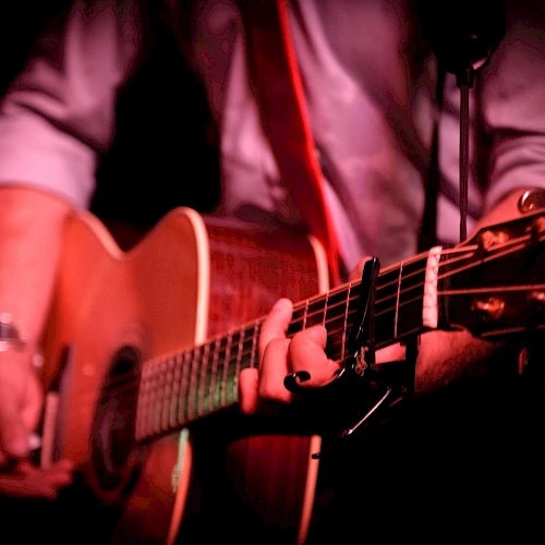 A person playing an acoustic guitar, close-up on hands strumming and fretboard under warm stage lighting.