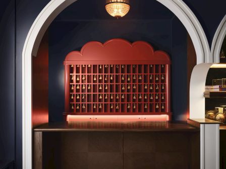 A lit display arch holds a red wall of hanging jewelry/bells with a glowing chandelier above, in a stylish shop room.