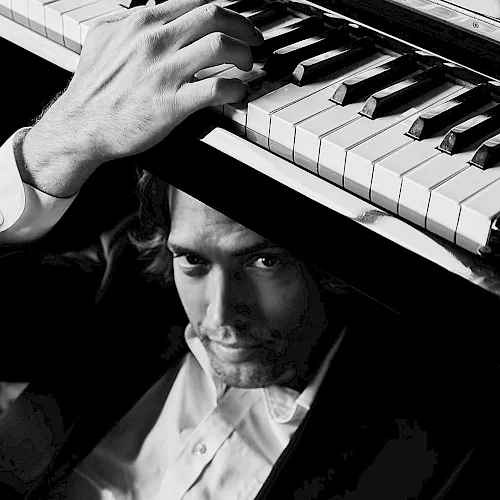 A man in a tuxedo plays a piano, his hand pressing the keys in a black-and-white shot.