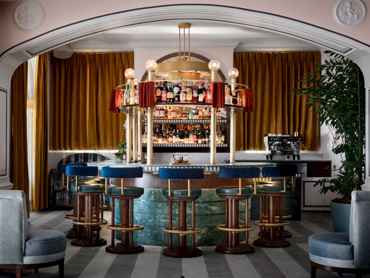 A stylish cocktail bar with a bottle-lined back bar, gold curtains, hanging globe lights, and tall stools.